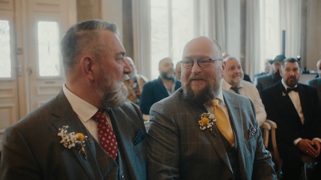 Video Reference N8: Event, Gentleman, Official, Person, Man, Indoor, Standing, Window, Suit, Holding, Looking, Couple, People, Woman, Table, Wedding, Glass, Wine, Room, Food, Shirt, Red, Group, City, Human face, Clothing, Glasses, Ceremony, Tie, Marriage, Smile, Senior citizen, Necktie