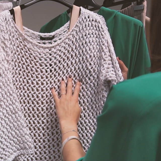 Video Reference N15: Clothing, Green, Sleeve, Neck, T-shirt, Shoulder, Design, Knitting, Pattern, Outerwear, Person, Indoor, Woman, Sitting, Cellphone, Phone, Holding, Table, Shirt, Head, White, Room, Blue, Man, Bed, Fashion accessory