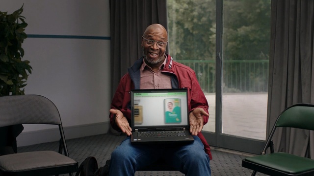 Video Reference N2: Sitting, Technology, Adaptation, Screenshot, Electronic device, Person, Indoor, Window, Computer, Laptop, Chair, Table, Desk, Man, Woman, Front, Looking, Room, Using, Keyboard, Young, Green, Holding, Living, People, Bed, Clothing, Human face
