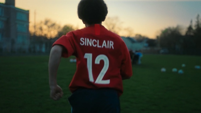 Video Reference N0: Red, Football player, Football, Green, Player, Youth, Sportswear, Standing, Jersey, Grass, Person, Outdoor, Game, Field, Soccer, Young, Holding, Playing, Ball, Man, Hand, Baseball, Boy, Wearing, Frisbee, Air, White, Flying, Sky, Clothing, Sports uniform, Athletic game