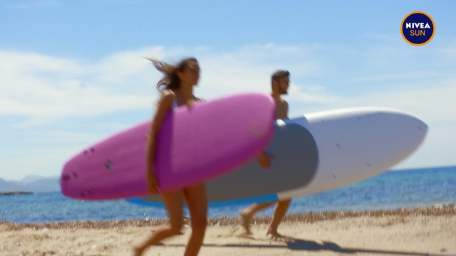 Video Reference N0: Surfboard, Surfing equipment, Sand, Pink, Inflatable, Surfing, Games, Summer, Fun, Beach, Outdoor, Water, Holding, Woman, Walking, Girl, Ocean, Board, Standing, Man, Carrying, Red, Blue, Wave, White, Frisbee, Sky, Shore