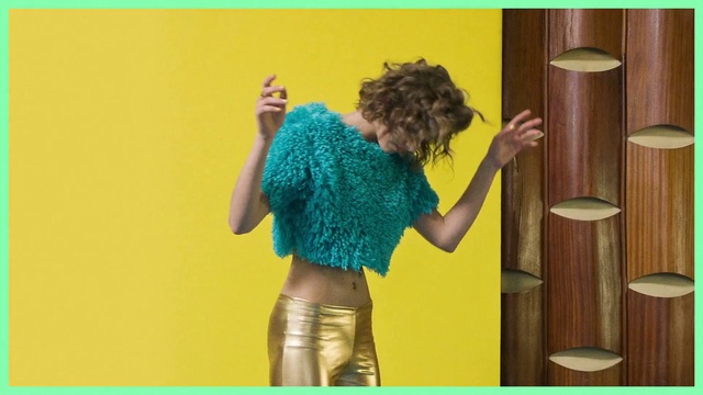 Video Reference N1: Green, Yellow, Textile, Costume, Person, Indoor, Standing, Front, Holding, Toy, Small, Woman, Young, Table, Man, Wearing, Room, Black, Phone, Shirt, Playing, Blue, Dance, Clothing, Girl, Skirt