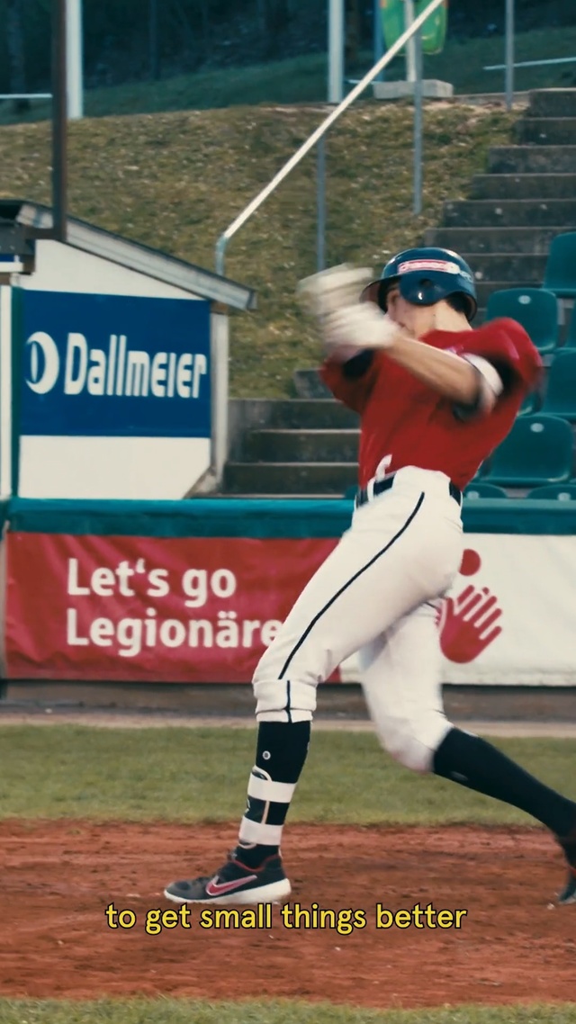 Video Reference N2: Baseball player, Sports, Baseball positions, Baseball park, Sport venue, Baseball uniform, Baseball equipment, Ball game, Baseball field, Bat-and-ball games, Person, Grass, Outdoor, Baseball, Player, Building, Ball, Field, Game, Swinging, Bat, Man, Batter, Playing, Pitch, Holding, Plate, Uniform, Standing, Crowd, Catcher, Air, People, Blue, White, Sports uniform, Sports equipment, Text, Clothing