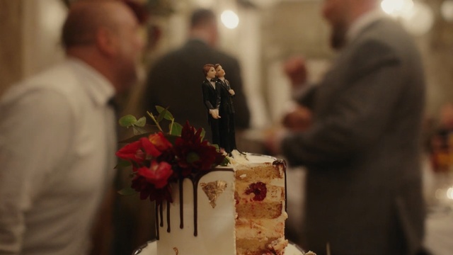 Video Reference N10: Wedding ceremony supply, Wedding cake, Cake, Event, Food, Ceremony, Tradition, Dessert, Icing, Torte, Person, Indoor, Table, Standing, Man, Woman, Front, Piece, Cut, Cutting, Holding, Wedding, Plate, Birthday, People, Young, Red, White, Group, Flower, Rose, Birthday cake, Candle, Vase