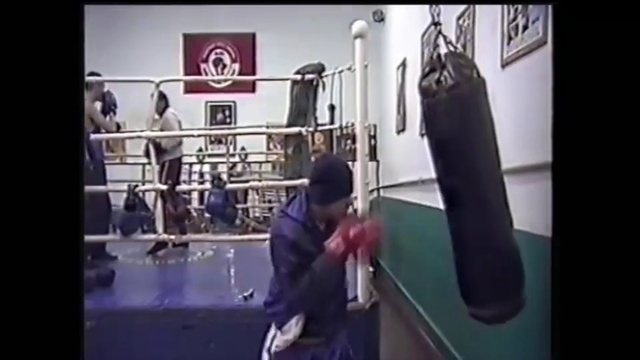 Video Reference N1: Boxing ring, Sport venue, Boxing, Striking combat sports, Contact sport, Boxing equipment, Individual sports, Combat sport, Punching bag, Sports equipment, Person, Indoor, Man, Front, Looking, Young, Standing, Small, Holding, Boy, Little, Woman, Wearing, Kitchen, Room, Computer, Playing, Cat, Text, Physical fitness, Wrestling, Exercise