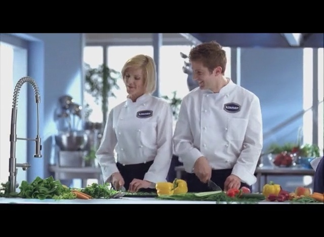 Video Reference N2: Cook, Chef, Chef uniform, Chief cook, Cooking, Uniform, Culinary art, Television program, Food, Cooking show, Person, Indoor, Window, Kitchen, Man, Table, Counter, Preparing, Woman, Standing, Wine, Sitting, Large, White, People, Holding, Cutting, Plate, Group, Restaurant, Chefs uniform, Meal