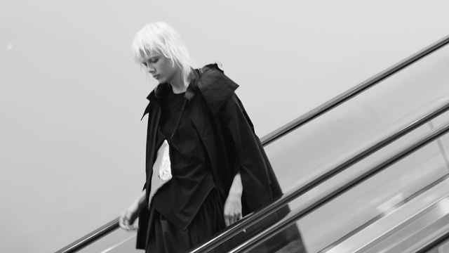 Video Reference N0: Black, Standing, Outerwear, Black-and-white, Photography, Cellist, Escalator, Bowed string instrument, Costume, Trench coat
