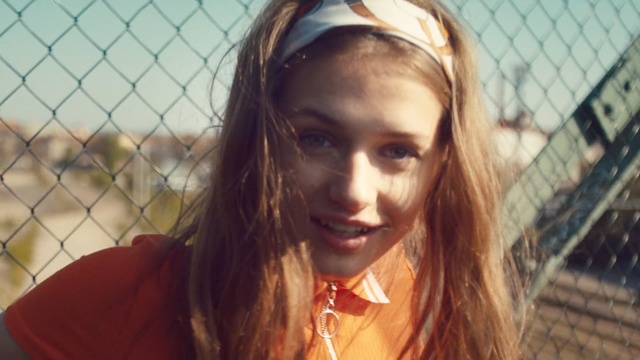 Video Reference N1: Hair, Face, Blond, Beauty, Eyebrow, Hairstyle, Lip, Long hair, Brown hair, Fun, Person, Fence, Woman, Outdoor, Holding, Looking, Wearing, Lady, Standing, Hand, Girl, Red, Young, Smiling, Shirt, Baseball, Phone, Hat, White, Human face, Smile, Selfie, Clothing, Portrait, Fashion accessory, Eyes
