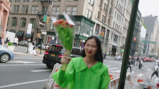 Video Reference N0: Green, Snapshot, Street, Pedestrian, Human, Holiday, Event, Fun, Road, Photography, Outdoor, Building, Person, City, Woman, Sidewalk, Holding, Man, Cross, Traffic, Standing, Walking, Busy, People, Hydrant, Riding, Phone, Car, Vehicle, Land vehicle, Clothing, Human face, Smile, Way
