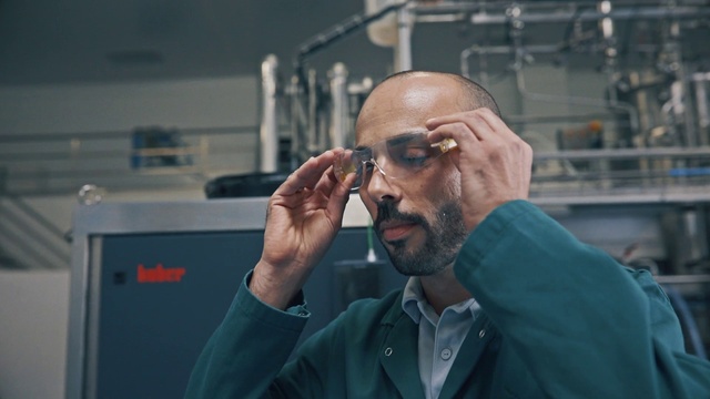 Video Reference N0: Glasses, Technology, Beard, Person, Man, Building, Cellphone, Phone, Front, Wearing, Looking, Holding, Standing, Mirror, Shirt, Talking, Sunglasses, Suit, Using, Computer, Table, Green, Hat, Room, Food, Blue, Human face, Clothing