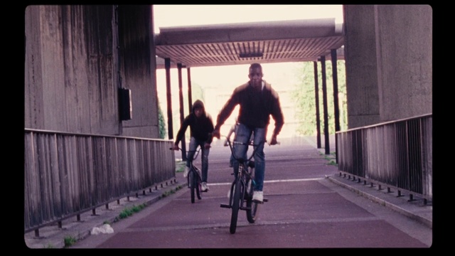 Video Reference N5: Cycling, Cycle sport, Bicycle, Vehicle, Recreation, Outdoor recreation, Road bicycle, Snapshot, Individual sports, Mode of transport, Person, Outdoor, Building, Man, Riding, Road, Board, Walking, Woman, Sidewalk, Young, Boy, Standing, Carrying, Bridge, Street, Wearing, Holding, Ramp, City, Doing, Train, Trick, Track, Bus, Bicycle wheel, Land vehicle, Wheel, Sports equipment, Bike, Bicycle helmet, Clothing