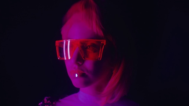 Video Reference N1: Purple, Light, Pink, Eyewear, Violet, Magenta, Visual effect lighting, Glasses, Neon, Fun, Person, Looking, Holding, Dark, Woman, Wearing, Man, Front, Shirt, Smiling, Red, Young, Standing, Sitting, Lit, White, Room, Large, Goggles, Sunglasses, Glass, Cake, Blue, Human face, Face, Spectacles