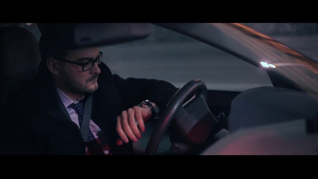 Video Reference N1: Automotive design, Eyewear, Luxury vehicle, Vehicle, Vehicle door, Driving, Car, Gentleman, Person, Man, Looking, Wearing, Holding, Sitting, Suit, Table, Red, Using, Glasses, Young, Standing, Phone, Hat, Human face, Screenshot, Clothing