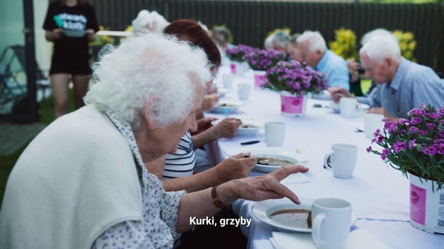 Video Reference N1: Grandparent, Event, Lunch, Meal, Plant, Flower, Floral design, Tableware, Person, Table, Food, Woman, People, Man, Looking, Standing, Sitting, Front, Cake, Eating, Group, Phone, Older, Cutting, Fruit, Plate, Sandwich, Holding, Laptop, Bowl, Crowd, White, Sheep, Wedding, Kitchen, Vase, Coffee cup