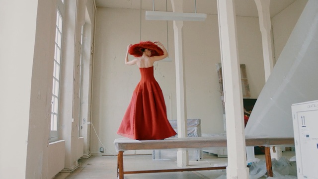 Video Reference N2: Red, Dress, Clothing, Gown, Standing, Room, Furniture, Outerwear, Floor, Interior design, Person