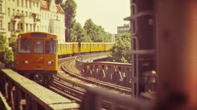 Video Reference N0: Transport, Mode of transport, Vehicle, Rolling stock, Railway, Train, Public transport, Track, Scale model, Railroad car, Outdoor, Building, Orange, Small, Sitting, Traveling, Bus, Platform, Street, Yellow, City, Side, Driving, Wooden, Old, Red, Parked, White, Station, Snow, Sign, Land vehicle, Railroad, Tree