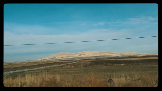 Video Reference N2: Grassland, Plain, Steppe, Sky, Prairie, Natural environment, Ecoregion, Horizon, Hill, Savanna, Outdoor, Grass, Mountain, Field, Sheep, Standing, Man, Cow, Horse, Train, Side, Track, Large, Grazing, Riding, Stop, White, Cattle, Red, Grassy, Herd, Blue, Board, Sign, Cloud, Landscape, Nature