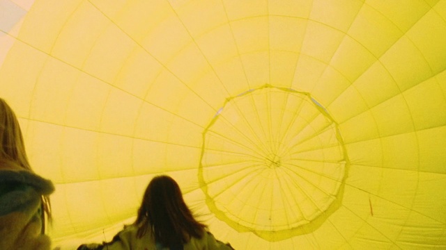 Video Reference N1: Yellow, Hot air balloon, Sky, Fun, Plant, Photography, Sunlight, Balloon, Vehicle, Leisure, Person, Indoor, Woman, Standing, Holding, Looking, Front, Umbrella, Young, Girl, Man, Mirror, Room, People, Phone, Playing, Laying, White