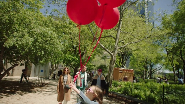 Video Reference N2: Red, Balloon, Tree, Party supply, Organism, Plant, Leisure, Adaptation, Architecture, Flower, Outdoor, Walking, Standing, Woman, Street, Holding, Young, Park, Man, Large, Wearing, Boy, Girl, Umbrella, Bear, Hat, Riding, Playing, People, Clothing, Outdoor object