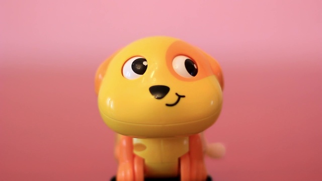 Video Reference N0: Yellow, Toy, Smile, Action figure, Animation, Smiley, Macro photography, Baby toys, Figurine, Indoor, Sitting, Small, Looking, Table, Monitor, Front, Orange, Computer, Little, Face, Desk, Mouse, Red, Ball, Bear, Keyboard, Pink, Wooden, Cake, Room, Holding, Remote, Food, White, Cartoon