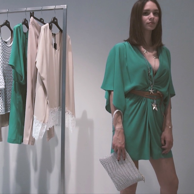 Video Reference N1: Clothing, Green, Clothes hanger, Dress, Day dress, Robe, Outerwear, Fashion design, Room, Sleeve, Person, Indoor, Woman, Standing, Wearing, Dressed, Man, Front, Holding, Young, Clothes, Walking, Shirt, White, Umbrella, Wall, Fashion, Coat, Handbag, Blouse, Skirt