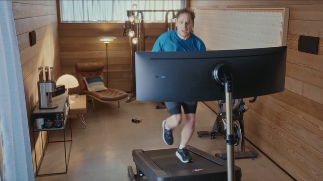 Video Reference N1: Desk, Standing, Treadmill, Exercise machine, Furniture, Exercise equipment, Table, Room, Computer desk, Electronic instrument, Person, Indoor, Sport, Living, Small, Sitting, Front, Computer, Mirror, Kitchen, Man, Dog, Laptop, Holding, Television, Young, Woman, Bed, Sink, White, Floor, Wall, Exercise device, Computer monitor