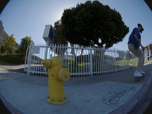 Video Reference N3: Yellow, Photography, Fisheye lens, Tree, Asphalt, World, Skateboarding, Recreation, Road, Road surface, Outdoor, Fence, Man, Object, Fire, Ramp, Hydrant, Riding, Doing, Side, Young, Park, Trick, Jumping, Boy, Railing, Board, Standing, White, Fire hydrant, Outdoor object