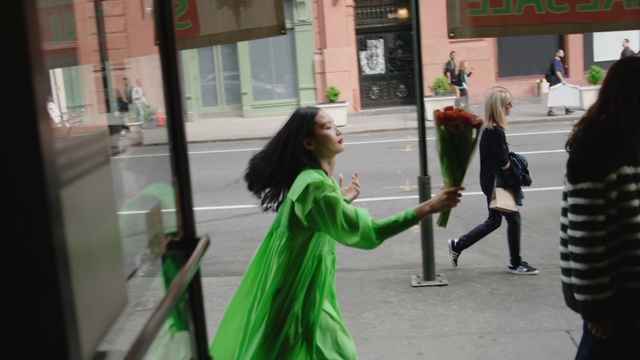 Video Reference N3: Green, Snapshot, Fun, Pedestrian, Street, Photography, Walking, Recreation, Holiday, Person, Building, Outdoor, Woman, Young, Girl, Holding, Front, Lady, Sidewalk, Standing, Little, Hair, Wearing, Hand, Shirt, City, Pizza, Phone, Red, Man, Dance, Clothing, Flower