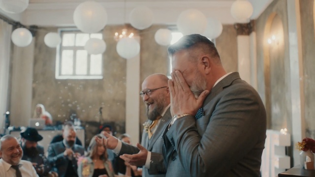 Video Reference N1: Photograph, Event, Photography, House, Ceremony, Person, Man, Indoor, Standing, Looking, Suit, Holding, Table, People, Older, Wine, Kitchen, Glass, Restaurant, Woman, Large, Food, Room, Board, Group, Wedding, Human face, Clothing, Marriage, Smile, Glasses, Crowd
