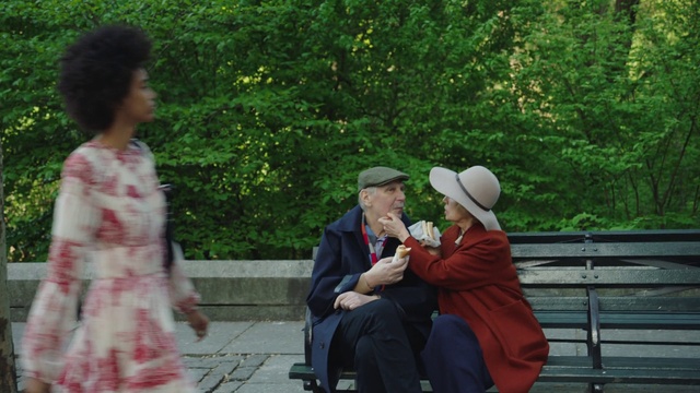 Video Reference N6: Botany, Sitting, Adaptation, Event, Leisure, Person, Outdoor, Bench, Park, Man, Child, Young, Woman, Boy, People, Holding, Game, Group, Red, Phone, Tree, Hat, Clothing, Fashion accessory, Sun hat, Fedora, Cowboy hat