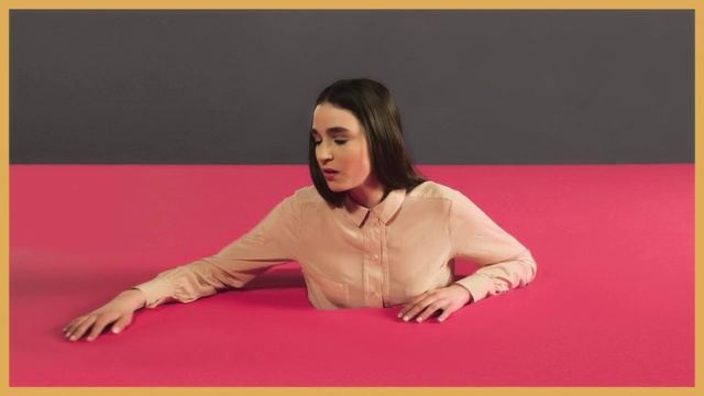 Video Reference N3: Pink, Arm, Sitting, Flooring, Leg, Joint, Human body, Table, Floor, Carpet, Person, Indoor, Woman, Ball, Girl, Bed, Television, Laying, Looking, Man, Young, Front, Large, Screen, Laptop, Holding, Room, Yellow, Rug, Text, Human face, Clothing, Furniture