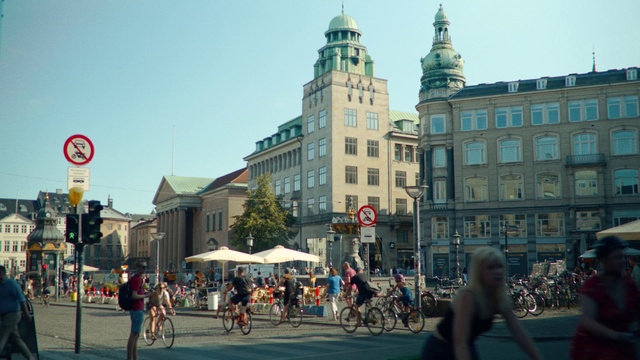 Video Reference N10: City, Town, Landmark, Urban area, Human settlement, Metropolitan area, Town square, Building, Downtown, Public space, Outdoor, Road, Street, Walking, People, Riding, Bicycle, Crossing, Man, Cross, Group, Woman, Traffic, Holding, Busy, Standing, Horse, Intersection, Large, Carriage, Old, Young, Drawn, Sign, Red, Crowd, Bus, Elephant, Sky, Vehicle, Land vehicle, Day